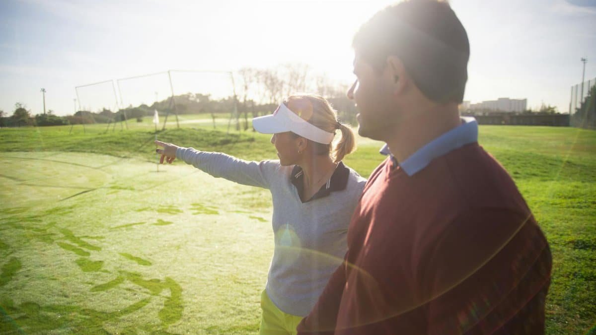 A man and woman communicating on a golf course, discussing strategy and enjoying the sunny day outdoors.
