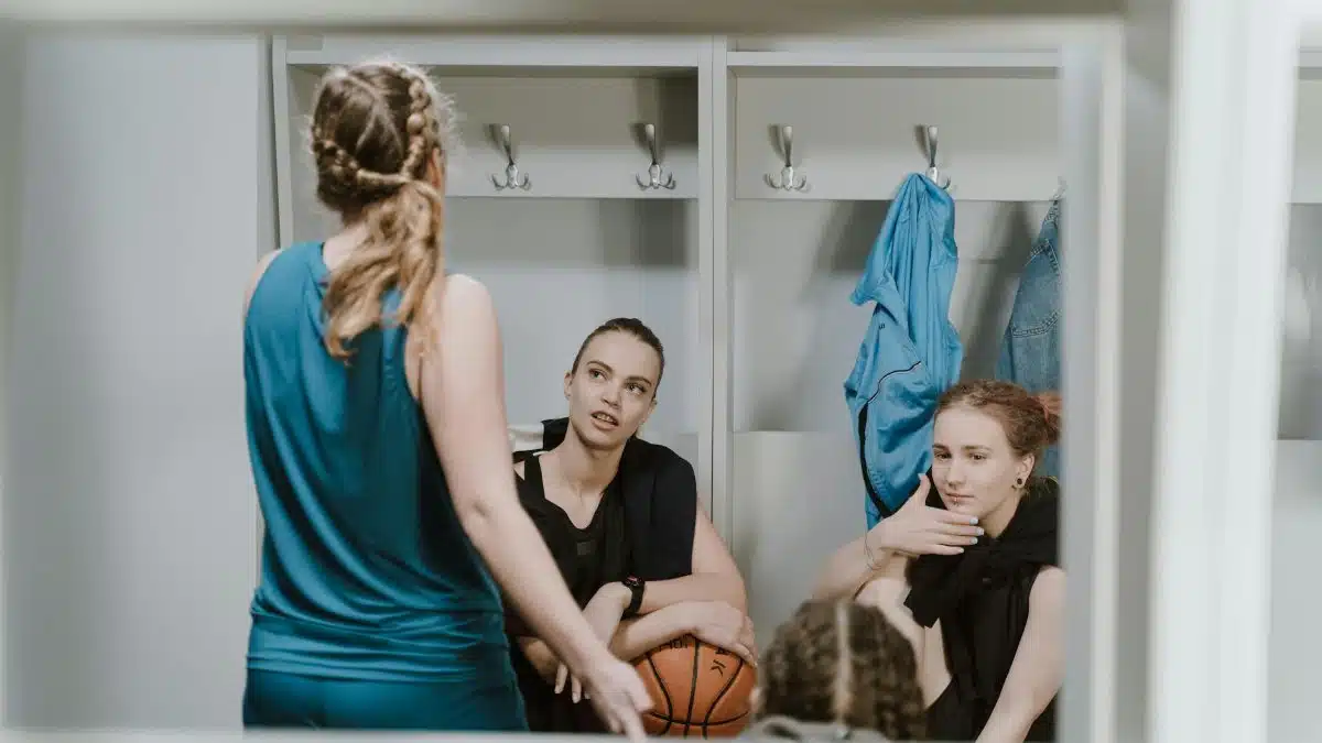 Three female basketball players share a discussion in a locker room ambiance portraying teamwork and sports spirit.