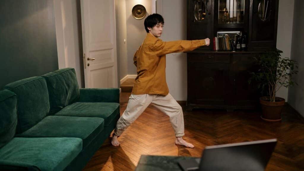 Adult practicing martial arts indoors, demonstrating skill and focus with a laptop nearby.