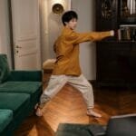 Adult practicing martial arts indoors, demonstrating skill and focus with a laptop nearby.