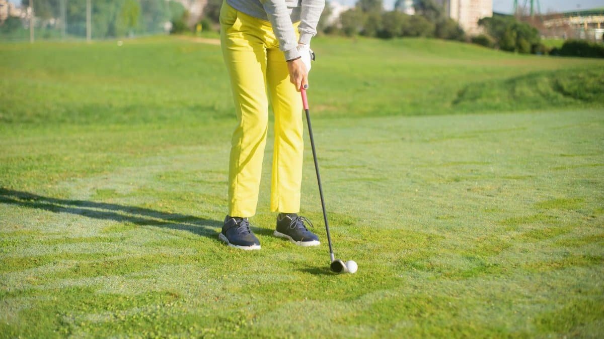 A golfer wearing yellow pants practices putting on a sunny day on a lush green course.