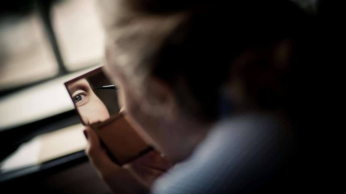 A woman intently applying eyeliner, captured in a reflective mirror close-up indoors.