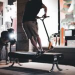 A videographer captures a scooter trick on a bench in front of an illuminated storefront at night.