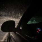 Capture of a car driving through a snowstorm at night, showing snow, road and dashboard lights.