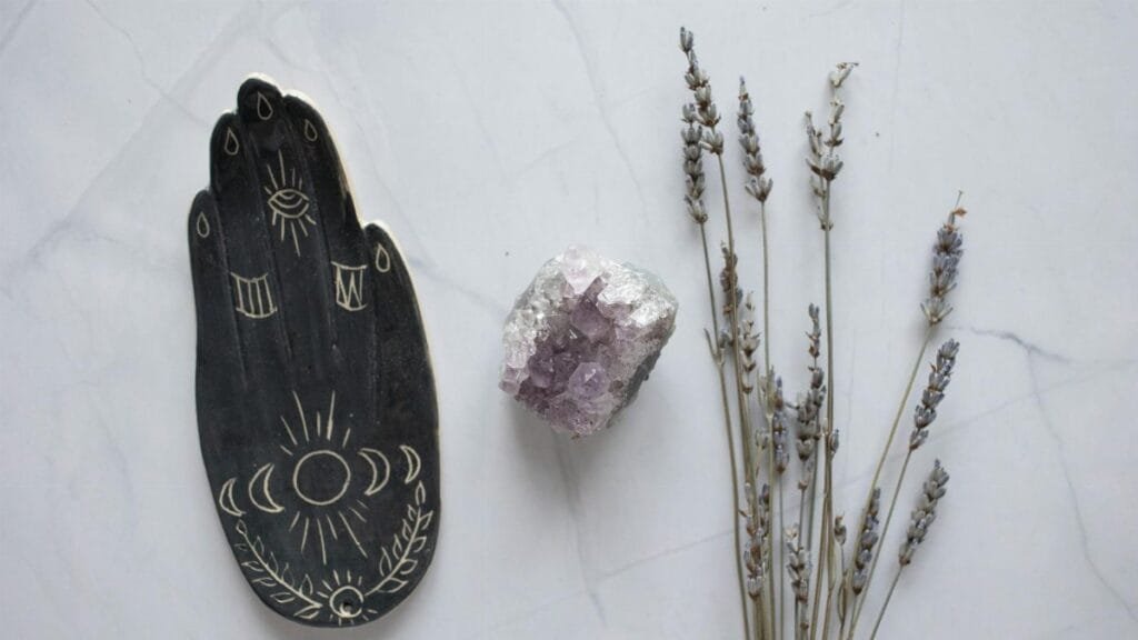 Flat lay of amethyst crystal and lavender sprigs with a decorative palm design on marble.
