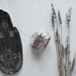 Flat lay of amethyst crystal and lavender sprigs with a decorative palm design on marble.