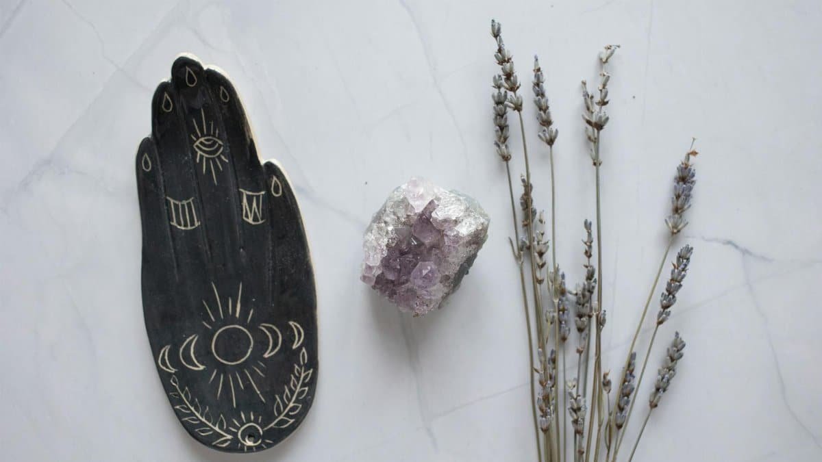 Flat lay of amethyst crystal and lavender sprigs with a decorative palm design on marble.