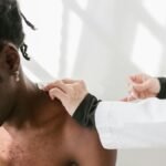 Close-up of a man receiving a shoulder massage for pain relief indoors.
