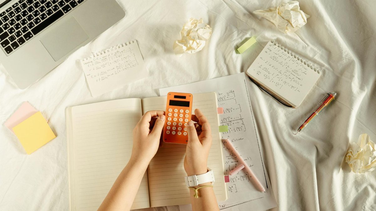 Flat lay of hands with orange calculator, notes, and laptop in a learning setting.