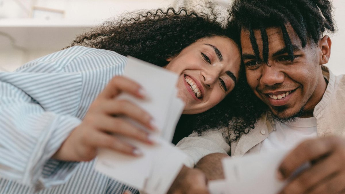 Smiling interracial couple enjoying memories together, looking at photos indoors. Warm and candid moment.