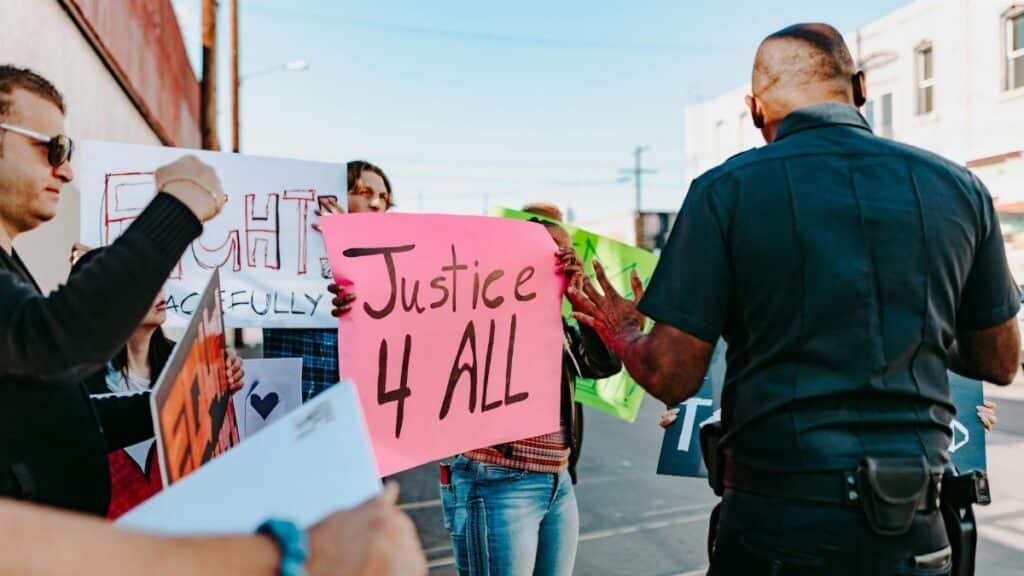 Police engaging with protesters holding signs for justice and peaceful rights.