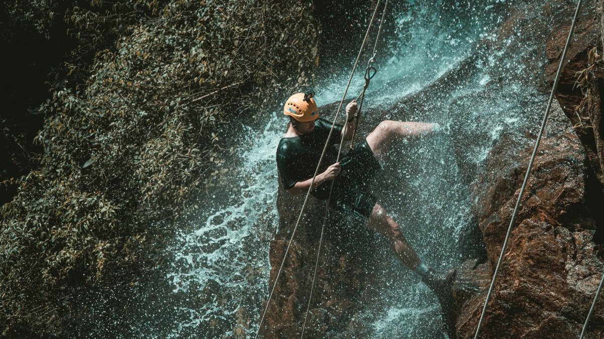 An adventurous person rappelling down a waterfall in a natural setting, showcasing outdoor excitement.