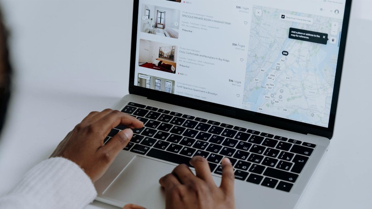 Hands typing on laptop searching Airbnb for accommodation options with map view.