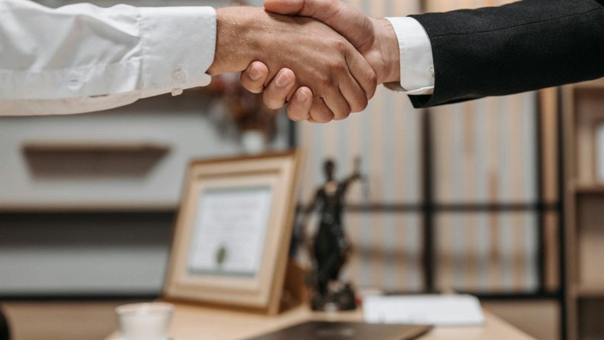 Close-up of a handshake between two professionals in a modern office setting, emphasizing partnership and agreement.