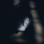 A dimly lit analog clock casting shadows, evoking a sense of mystery and time passage.
