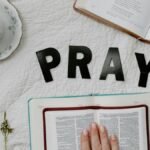 Flat lay of morning prayer routine including Bible, coffee, and 'PRAY' letters.