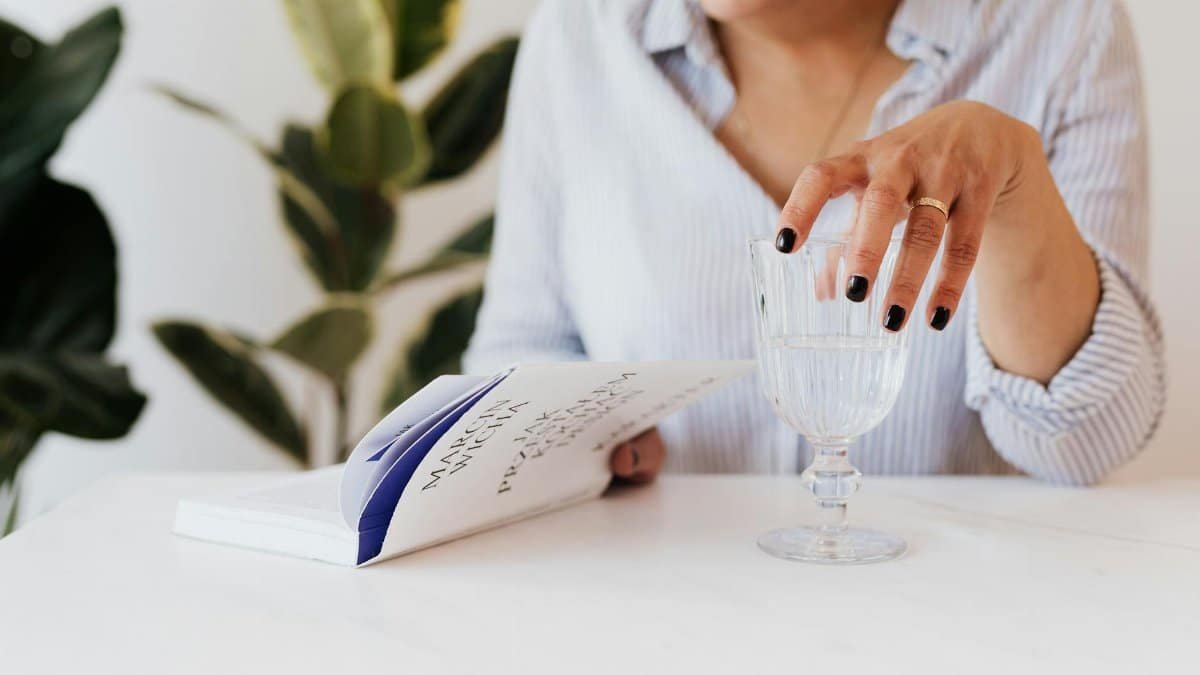 Woman reading a book while sipping water, enjoying a peaceful indoor setting.