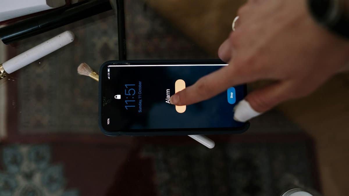 Close-up of a person touching a smartphone alarm screen with makeup items nearby.