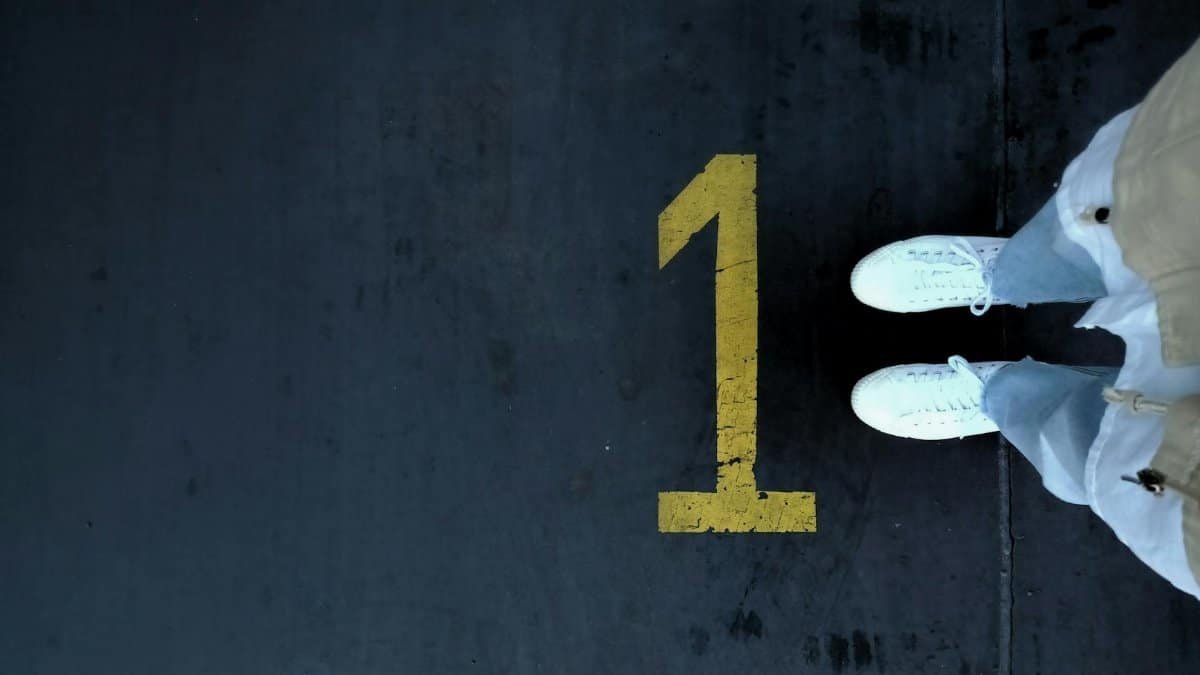 Aerial shot of white sneakers on a dark surface with a painted yellow number one.