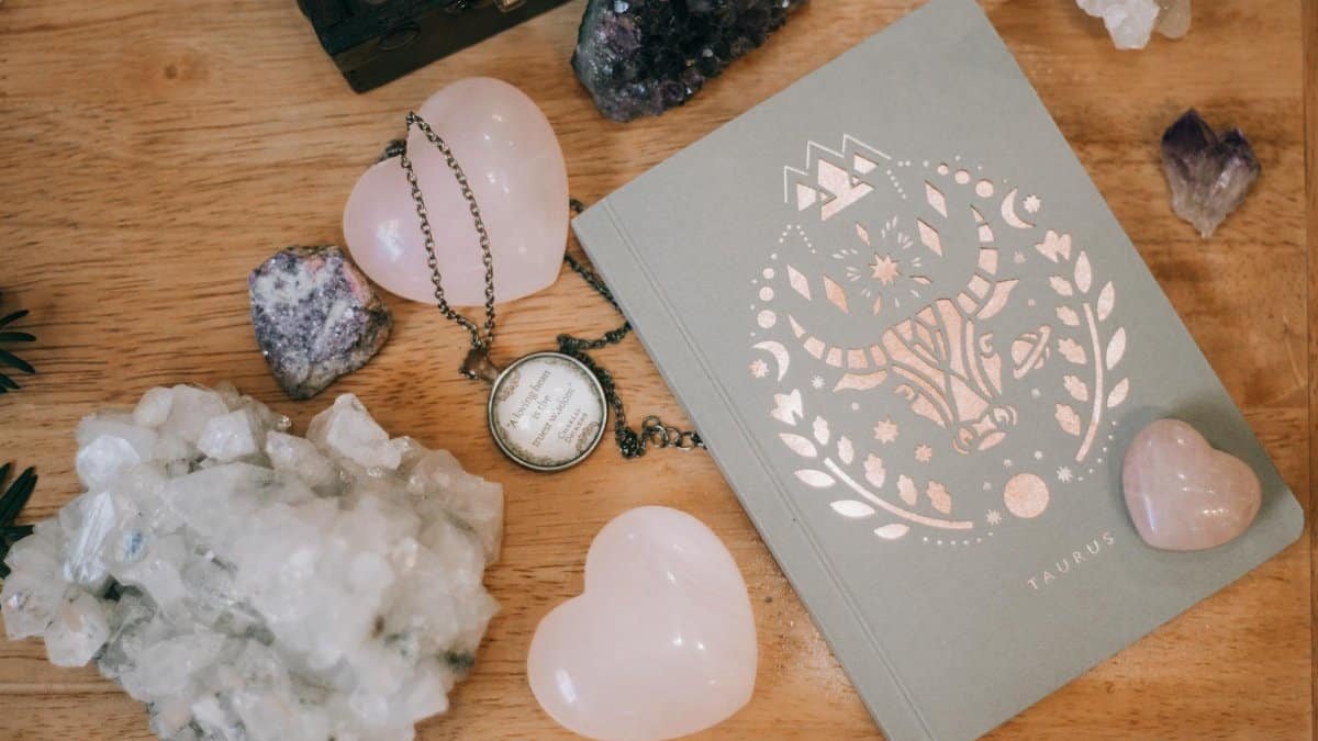 Taurus-themed notebook surrounded by heart-shaped and raw crystals on a wooden surface, evoking tranquility.