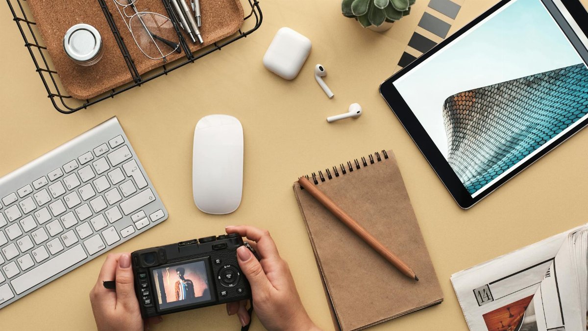 Overhead view of a modern workspace featuring tech gadgets, a camera, and a notepad.