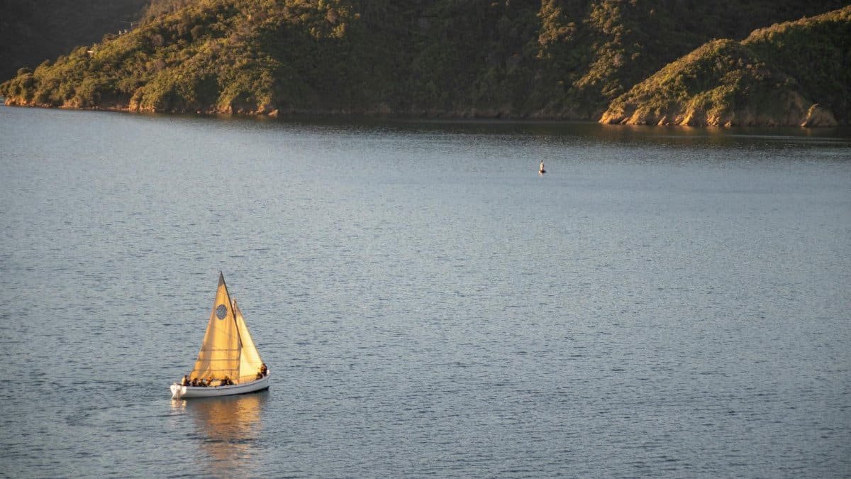A serene scene of a sailboat gliding on a tranquil lake with lush hills at sunset.