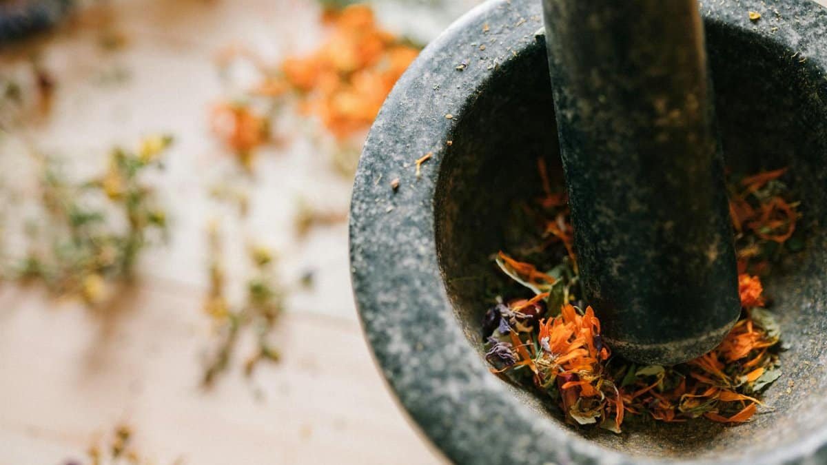 Close-up of a stone mortar and pestle grinding vibrant dried flowers on a wooden surface.