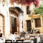A quiet outdoor cafe in Chania, Greece, under sunlight and vibrant flowers.