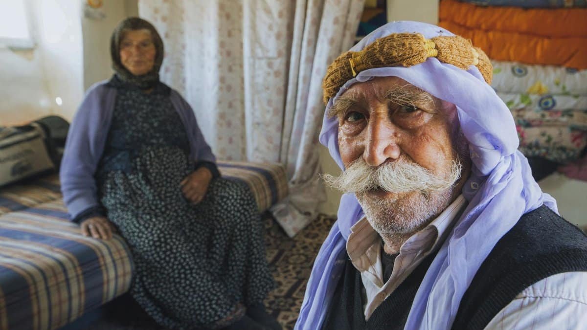 Senior couple in traditional Middle Eastern clothing inside a cozy home setting.