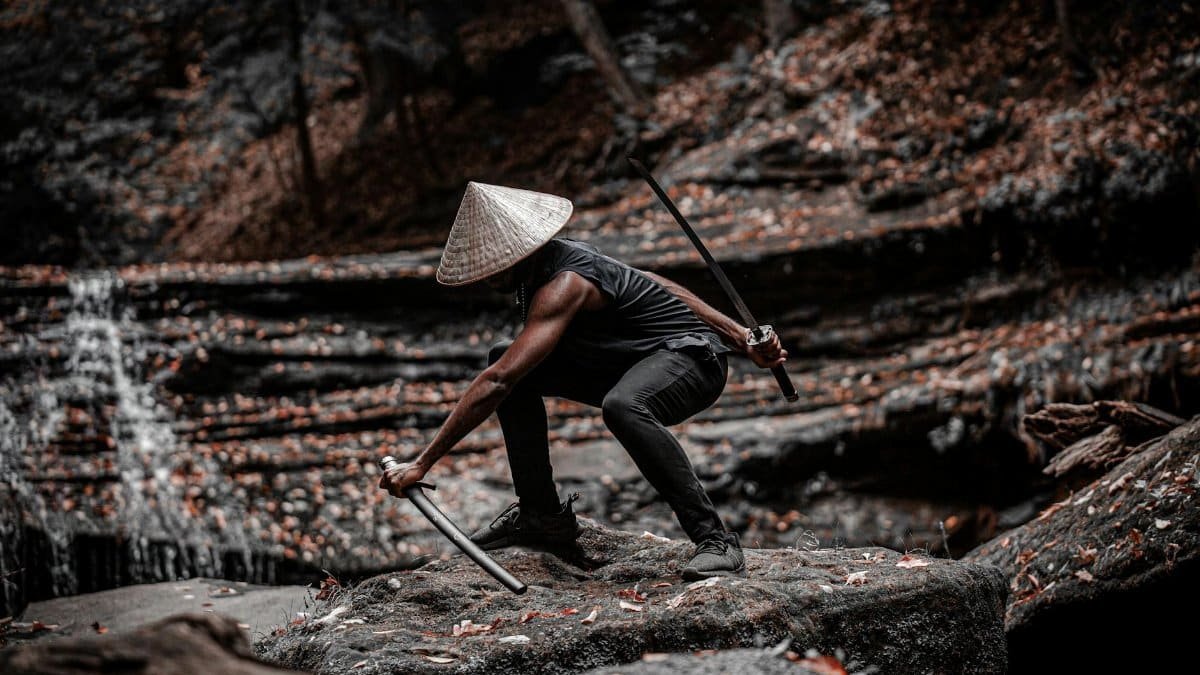 A lone samurai crouches with a sword in a serene forest setting, exuding strength and focus.