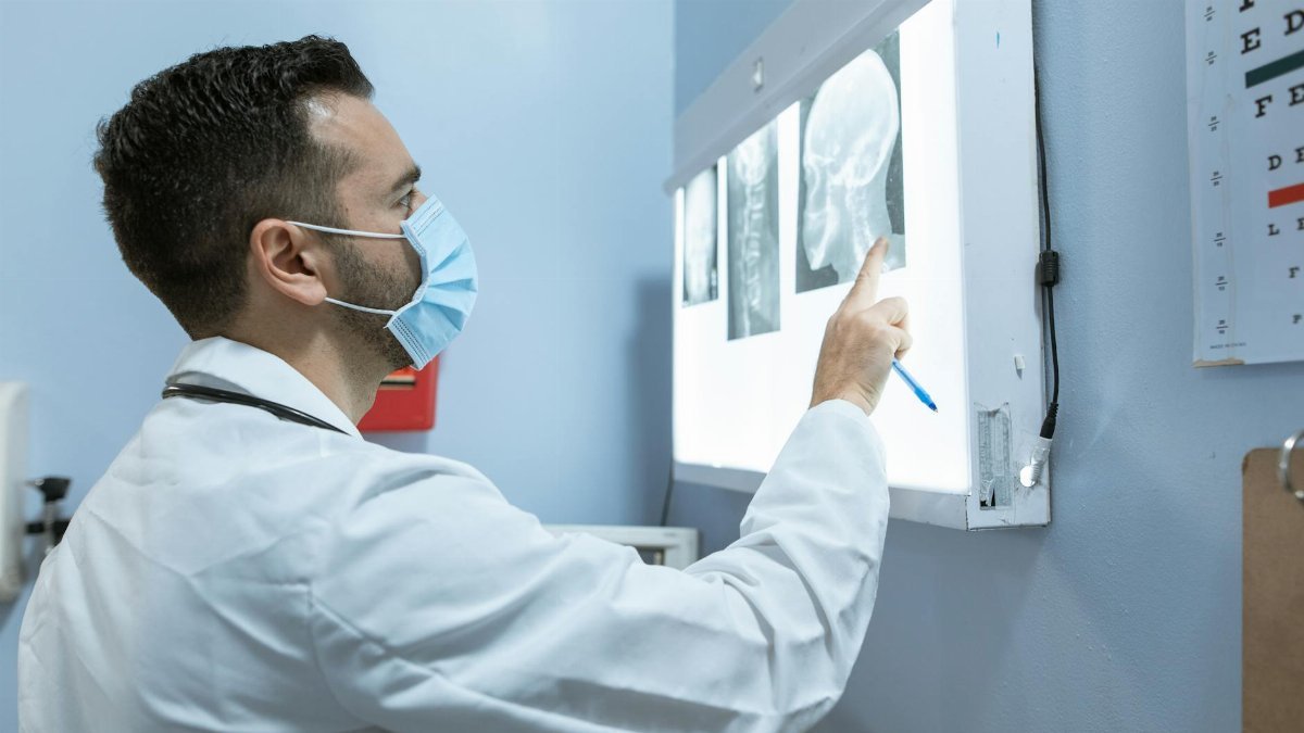 A healthcare professional examines brain X-rays while wearing a face mask in a hospital setting.