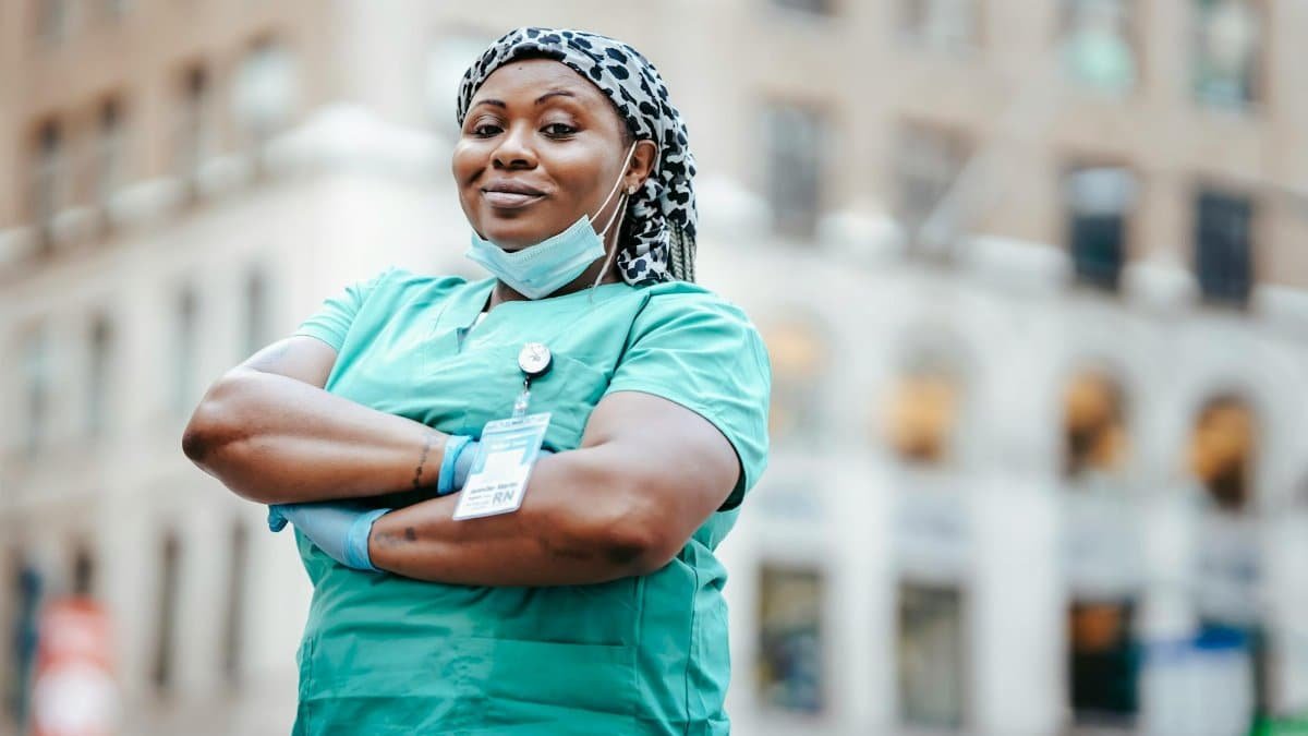 Proud nurse with arms crossed, in uniform, outdoors, urban setting, showing confidence and professionalism.