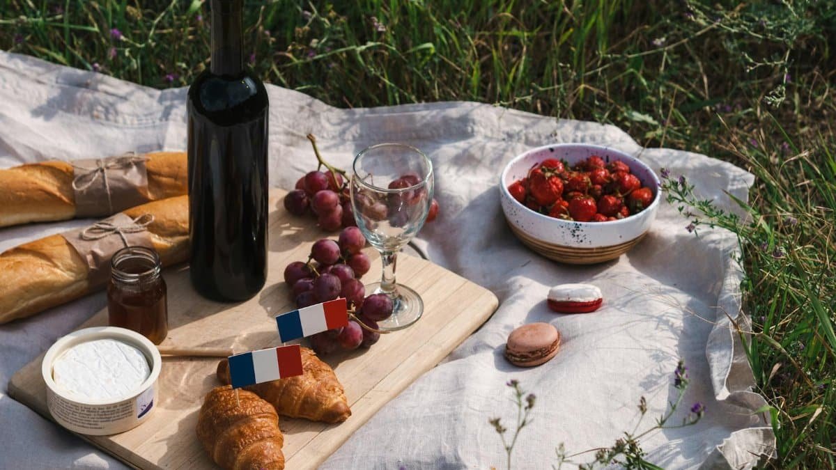 A delightful outdoor French picnic setup featuring baguettes, wine, and a variety of fresh foods.