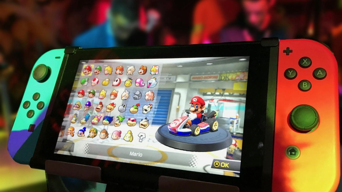 Close-up of a Nintendo Switch showing Mario Kart selection screen, gaming atmosphere in the background.