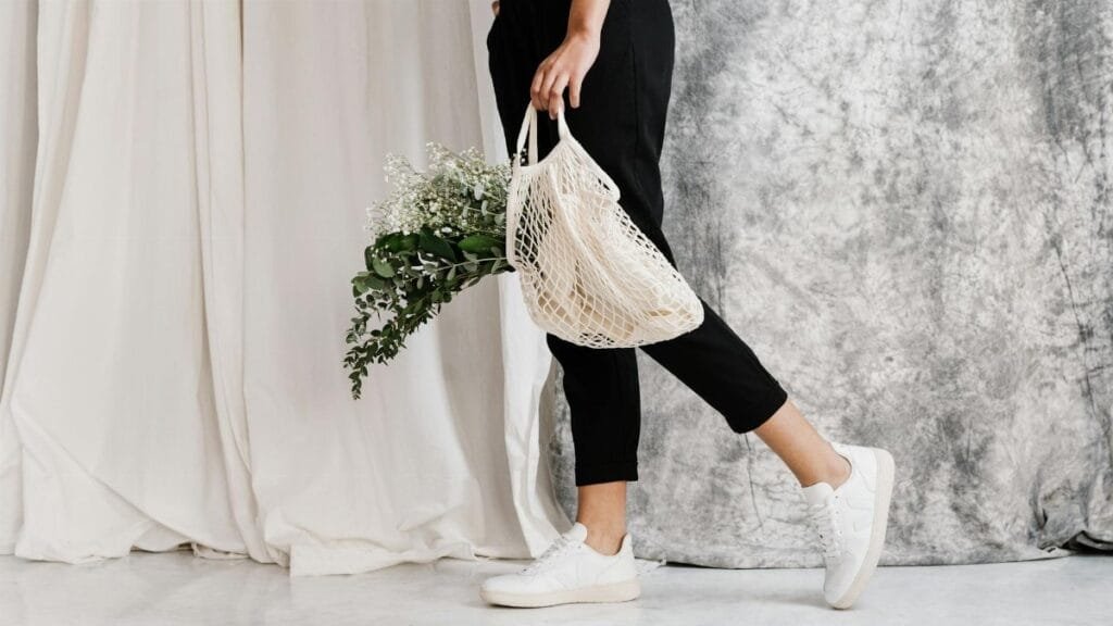Woman in minimalist outfit holding an eco-friendly mesh bag filled with flowers, showcasing sustainable fashion.