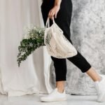 Woman in minimalist outfit holding an eco-friendly mesh bag filled with flowers, showcasing sustainable fashion.