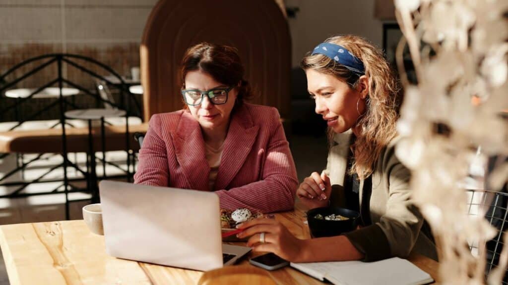 Two women working together on a laptop in a cozy café setting.