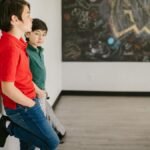 Two boys leaning against a wall in a classroom with graffiti board.