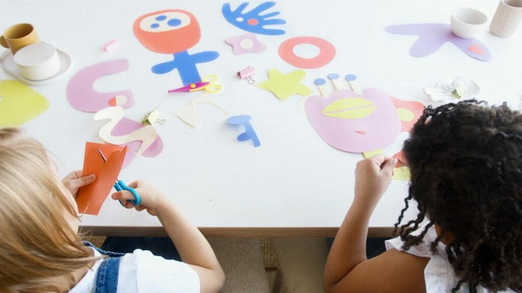Two children enjoying an art class with colorful paper cutouts, fostering creativity and fun.