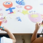 Two children enjoying an art class with colorful paper cutouts, fostering creativity and fun.