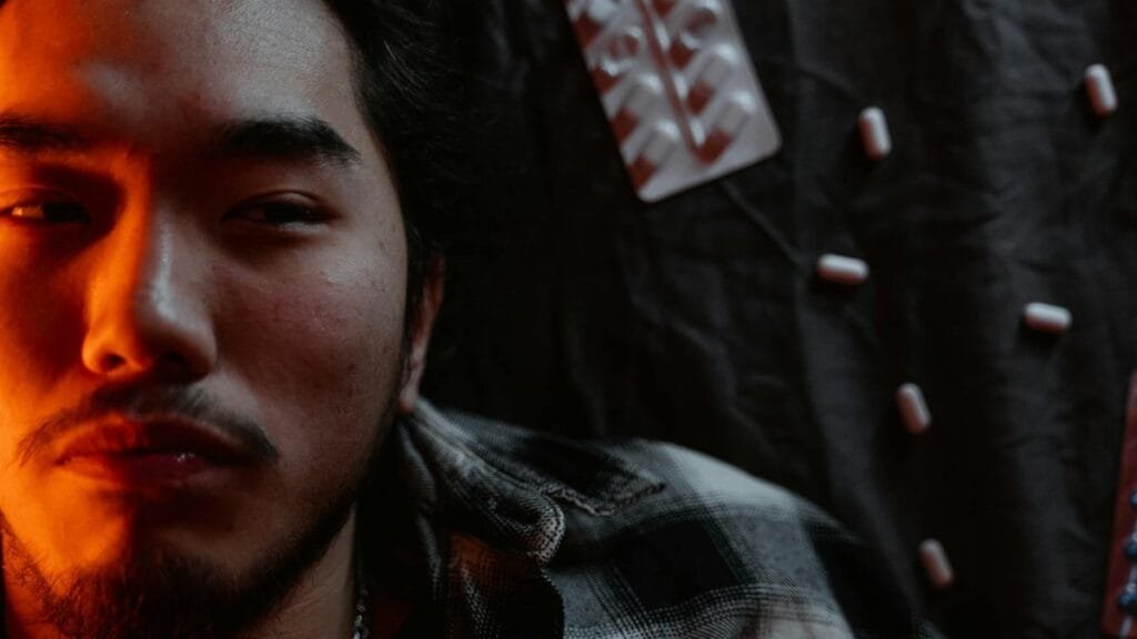 Close-up of a man's face with a dramatic light, surrounded by pills, conveying anxiety.