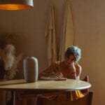 A senior woman enjoys journaling at a table in a warm, cozy home setting.