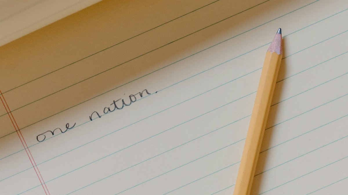 A minimalistic image featuring a pencil on a lined notebook with handwritten 'one nation'.
