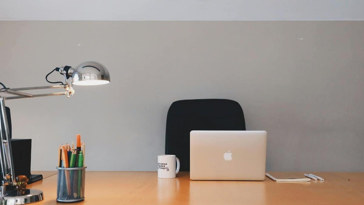 A tidy minimalist office setup featuring a laptop, desk lamp, and stationery.