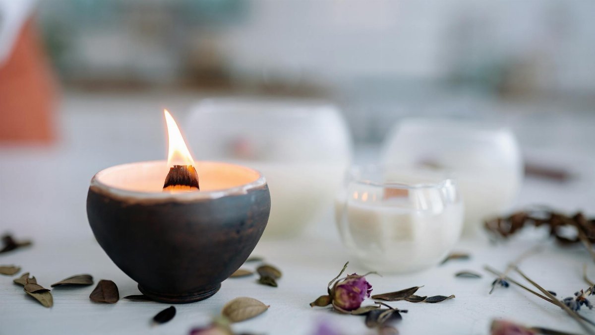 Warm candle flame in ceramic holder with dried flowers on table.