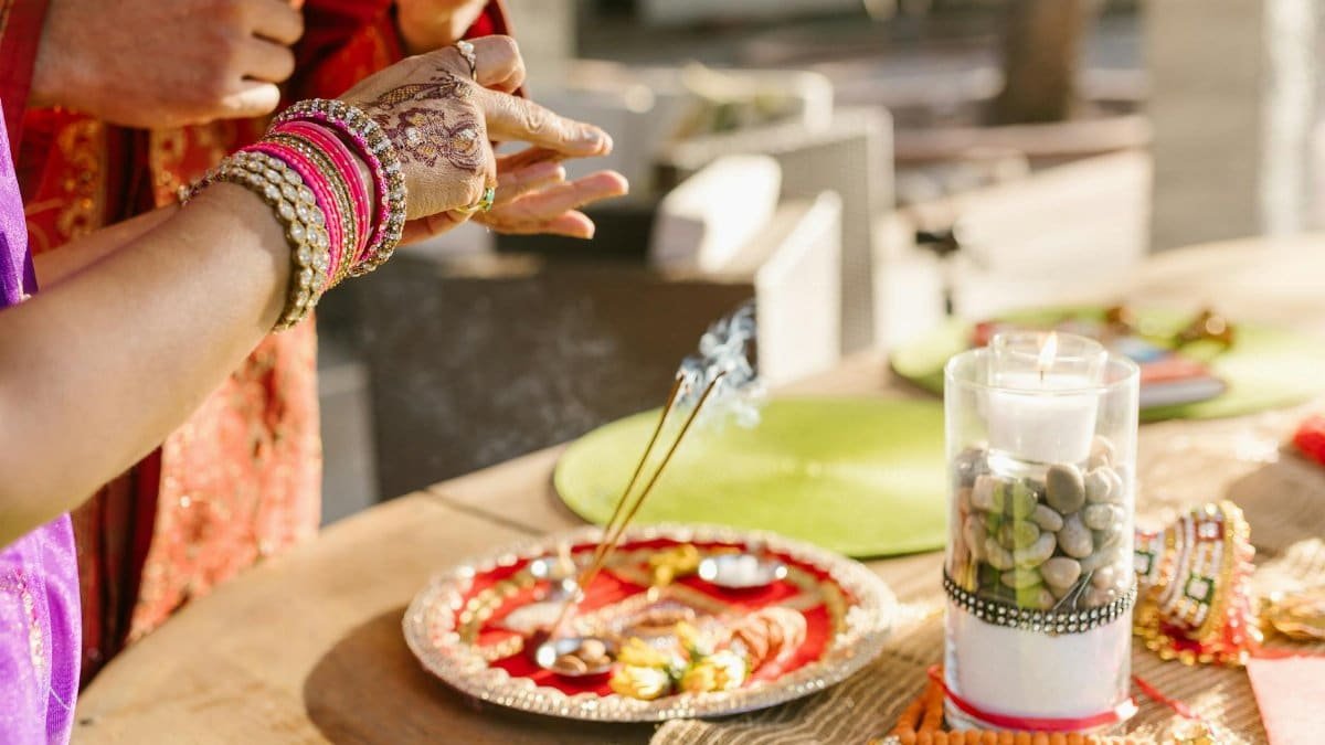 Vibrant Indian ritual setup with candle, incense, and festive elements on a decorated plate.