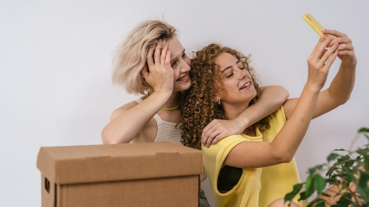 Lesbian couple smiling and taking a selfie while moving into a new apartment, filled with joy and togetherness.