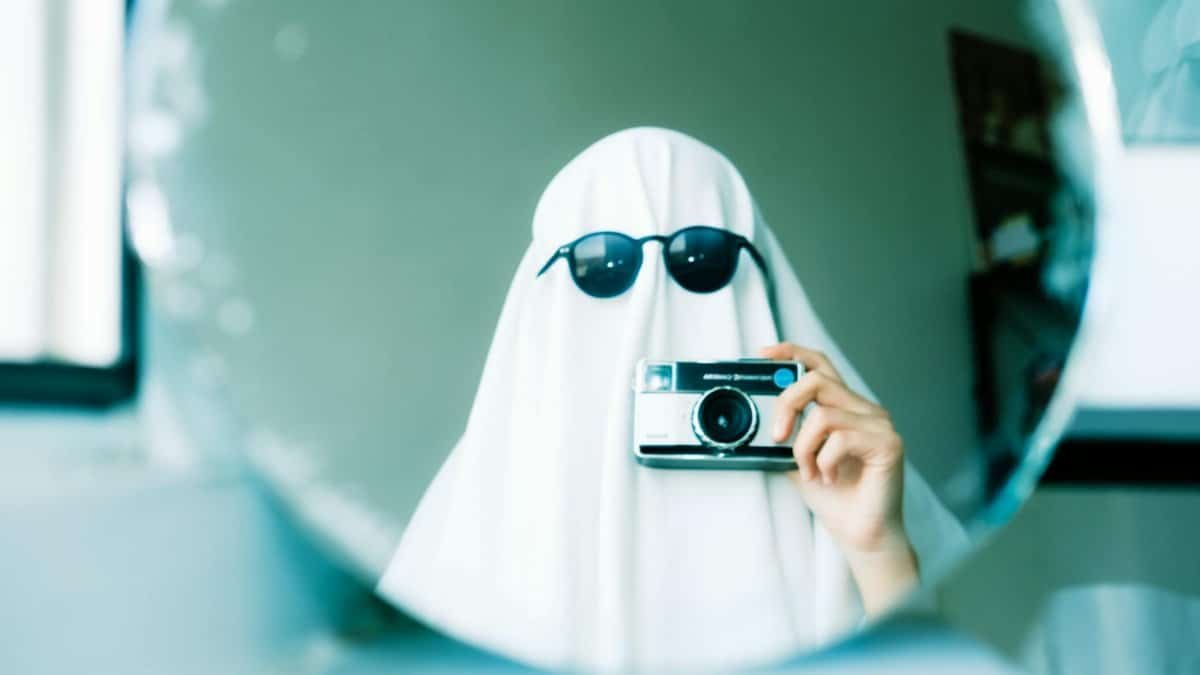 Imaginative Halloween ghost costume using a sheet and sunglasses, holding a camera in front of a mirror.