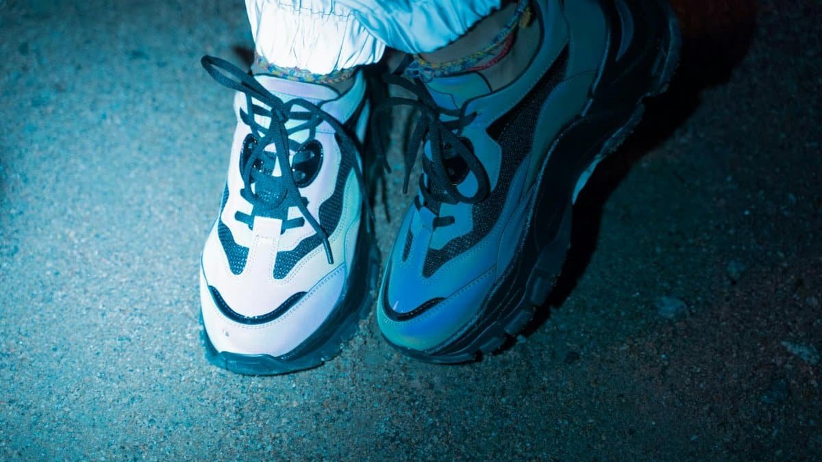 Stylish sneakers with lace ties lit by spotlight on a dirt ground at night.