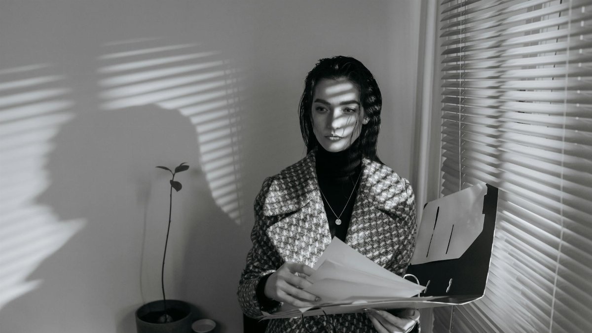 Business woman in black and white, reviewing documents with blinds creating shadows.